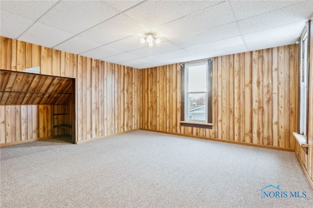 unfurnished room featuring carpet, a paneled ceiling, and wooden walls