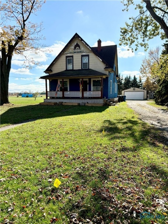 view of front of property featuring covered porch, a garage, an outbuilding, and a front yard