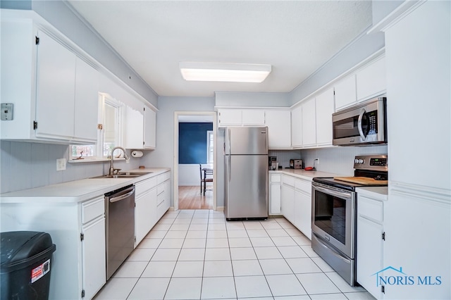 kitchen with appliances with stainless steel finishes, sink, light tile patterned floors, and white cabinets