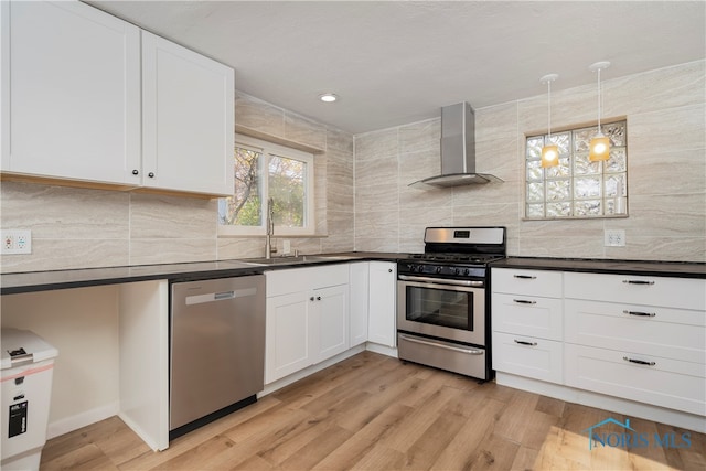 kitchen with stainless steel appliances, white cabinetry, sink, wall chimney range hood, and light wood-type flooring