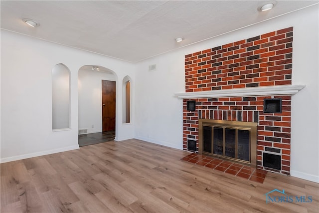 unfurnished living room featuring a brick fireplace, a textured ceiling, and light hardwood / wood-style flooring