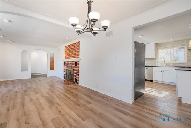 unfurnished living room featuring a fireplace, a chandelier, sink, and light wood-type flooring