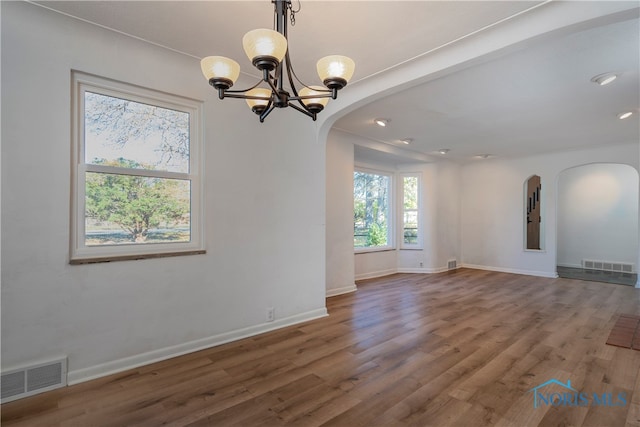 empty room featuring wood-type flooring and an inviting chandelier