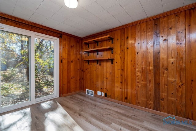 unfurnished room with light wood-type flooring and wooden walls