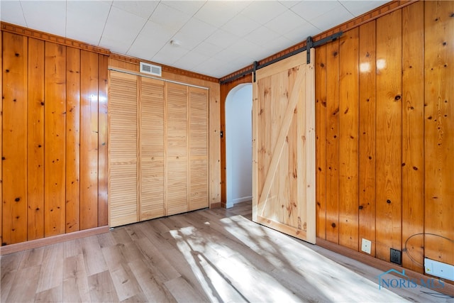 unfurnished bedroom featuring light wood-type flooring, a barn door, and wooden walls