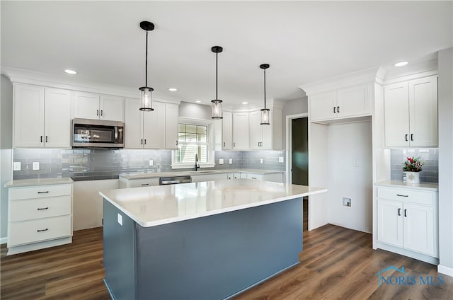 kitchen with white cabinets, appliances with stainless steel finishes, a kitchen island, and dark wood-type flooring