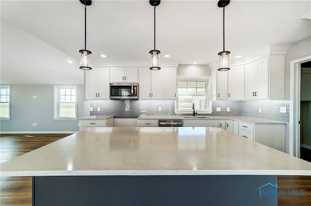 kitchen featuring white cabinets, decorative light fixtures, a kitchen island, and appliances with stainless steel finishes