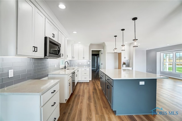 kitchen featuring stainless steel appliances, sink, decorative light fixtures, white cabinets, and a kitchen island