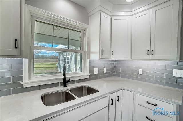 kitchen with white cabinets, light stone counters, sink, and tasteful backsplash