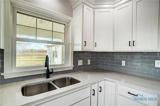 kitchen featuring light stone countertops, white cabinetry, sink, and tasteful backsplash