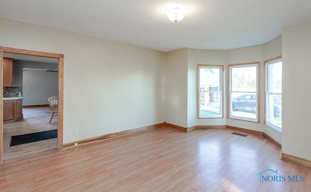 empty room featuring a textured ceiling and light hardwood / wood-style floors