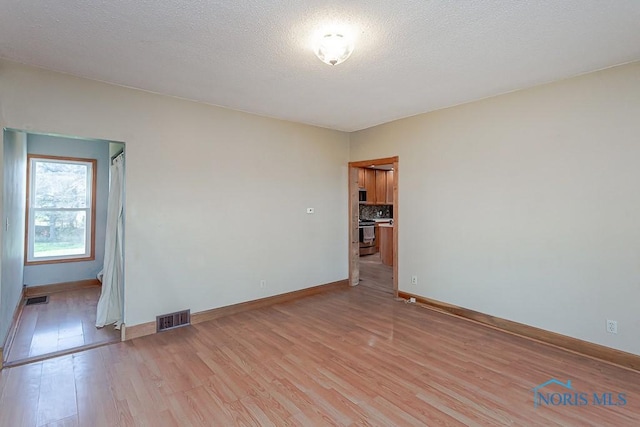 empty room with light wood-type flooring and a textured ceiling