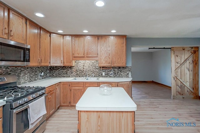 kitchen featuring light wood-type flooring, tasteful backsplash, stainless steel appliances, sink, and a barn door