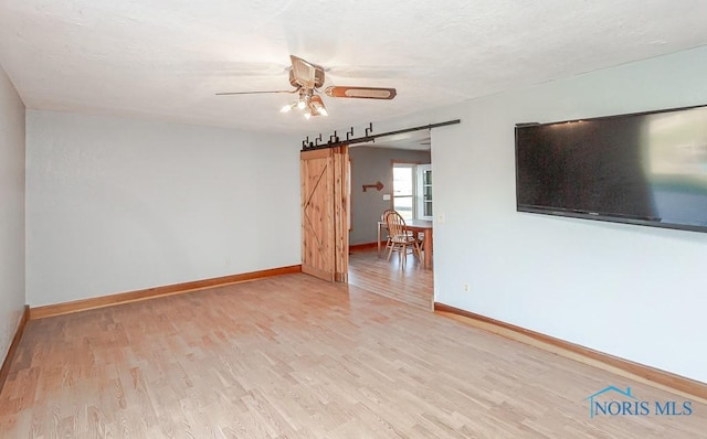 spare room with a barn door, light hardwood / wood-style flooring, and ceiling fan