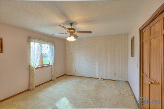 unfurnished bedroom with light carpet, a textured ceiling, a closet, and ceiling fan