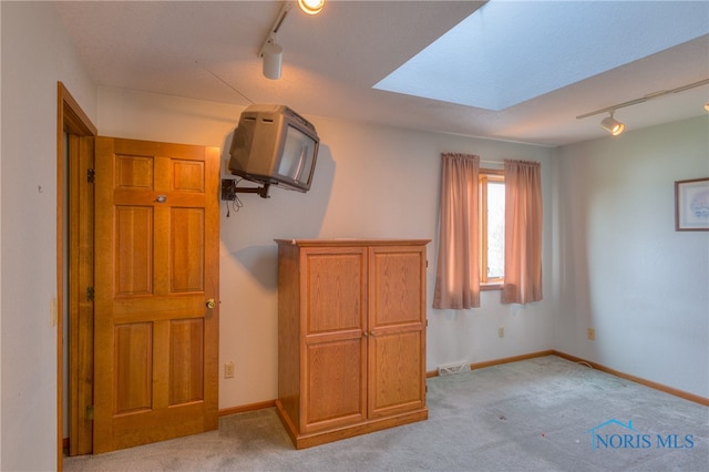 unfurnished bedroom featuring a skylight, rail lighting, and light colored carpet