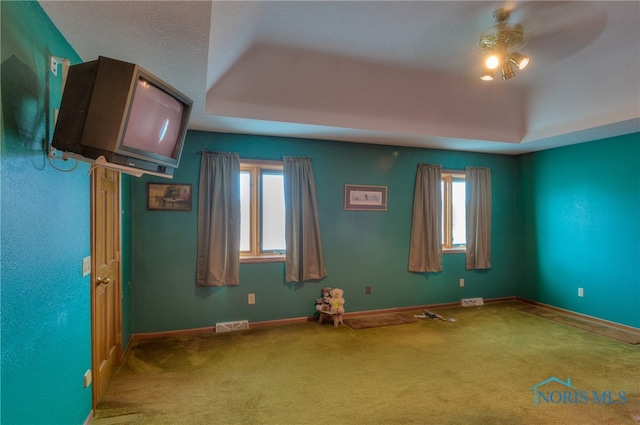 carpeted empty room featuring ceiling fan, a healthy amount of sunlight, and a tray ceiling