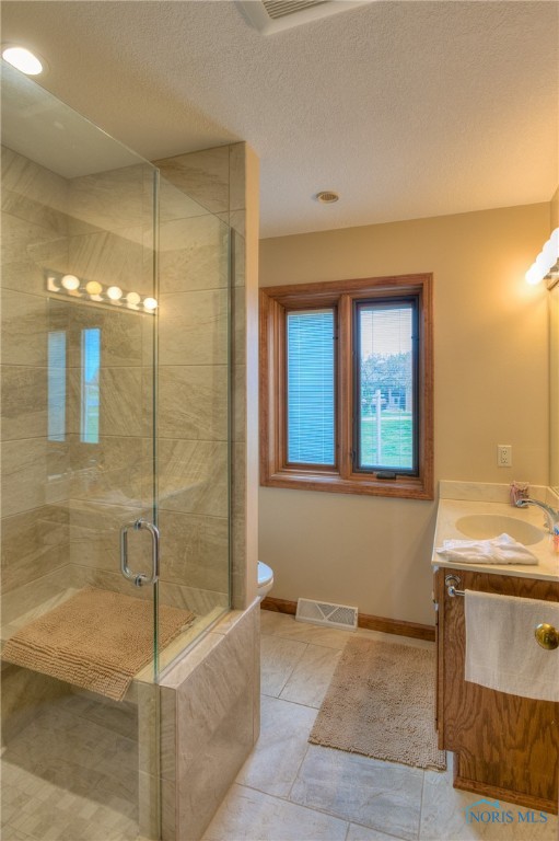 bathroom featuring tile patterned flooring, a textured ceiling, toilet, a shower with door, and vanity