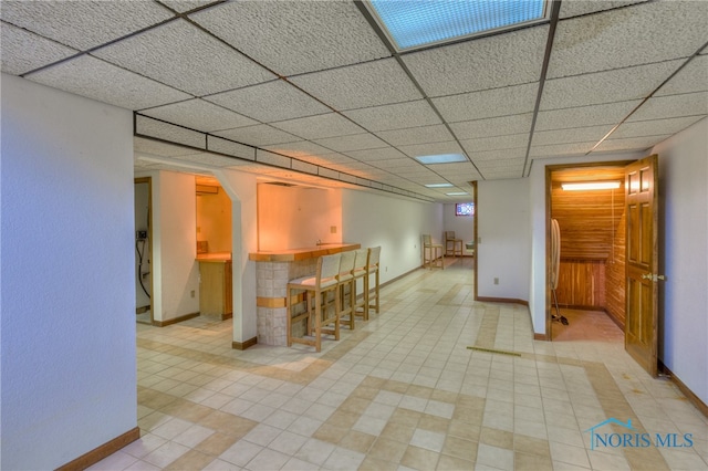 interior space featuring a kitchen breakfast bar, a drop ceiling, and light tile patterned flooring