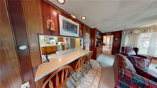 kitchen with stainless steel dishwasher, wooden walls, and light carpet