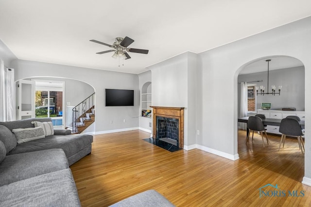 living room featuring built in features, hardwood / wood-style flooring, and ceiling fan with notable chandelier