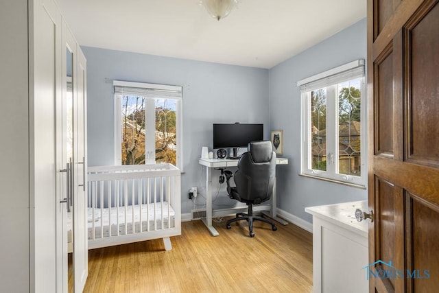 bedroom featuring a crib, light hardwood / wood-style floors, and multiple windows