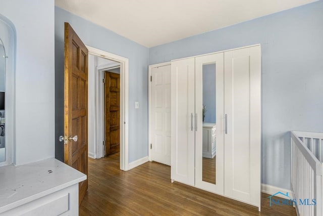 unfurnished bedroom featuring dark wood-type flooring, a crib, and a closet