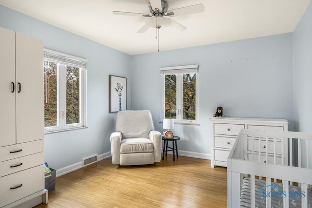 bedroom featuring a crib, light hardwood / wood-style flooring, multiple windows, and ceiling fan