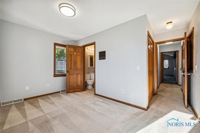 unfurnished bedroom featuring light colored carpet and ensuite bath