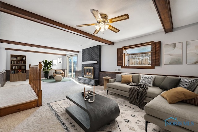 living room featuring a fireplace, light carpet, ceiling fan, and beam ceiling