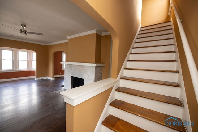 stairs featuring crown molding, ceiling fan, a fireplace, and wood-type flooring