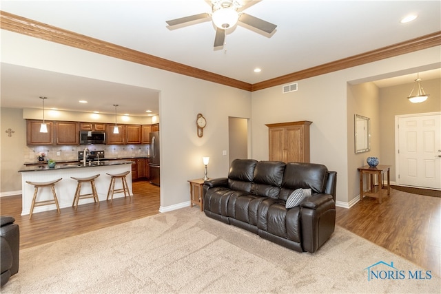 living room featuring ornamental molding, light wood-type flooring, ceiling fan, and sink