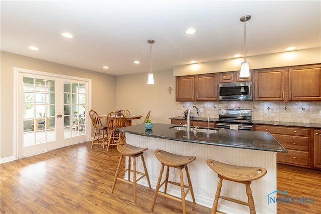 kitchen with a center island with sink, appliances with stainless steel finishes, pendant lighting, sink, and light hardwood / wood-style floors