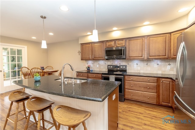 kitchen with stainless steel appliances, sink, a kitchen island with sink, a breakfast bar, and pendant lighting