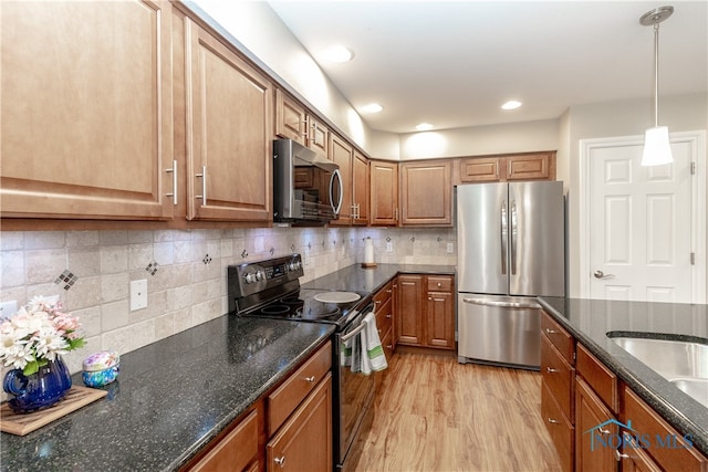 kitchen with stainless steel appliances, dark stone counters, pendant lighting, and light hardwood / wood-style flooring