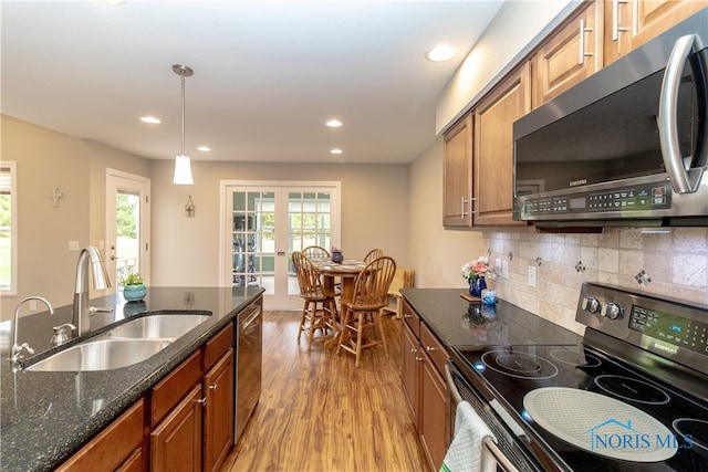 kitchen featuring appliances with stainless steel finishes, hanging light fixtures, sink, light hardwood / wood-style floors, and dark stone countertops