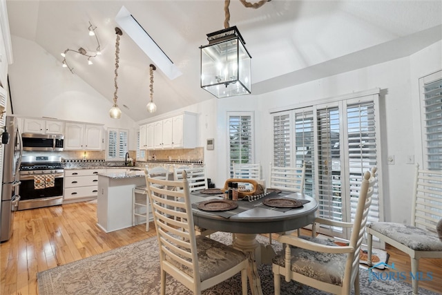 dining area featuring light hardwood / wood-style floors, sink, high vaulted ceiling, and an inviting chandelier