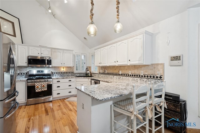 kitchen featuring tasteful backsplash, stainless steel appliances, light hardwood / wood-style flooring, white cabinets, and hanging light fixtures