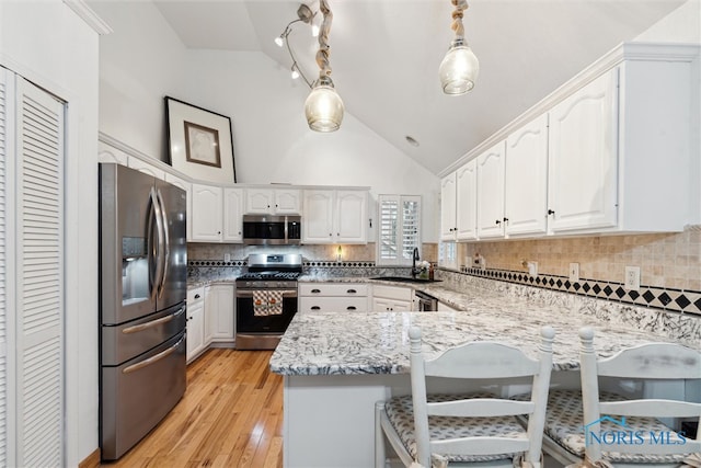 kitchen with kitchen peninsula, appliances with stainless steel finishes, pendant lighting, white cabinets, and light hardwood / wood-style floors