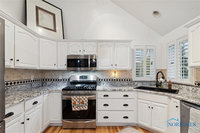 kitchen featuring lofted ceiling, backsplash, sink, white cabinetry, and stainless steel appliances