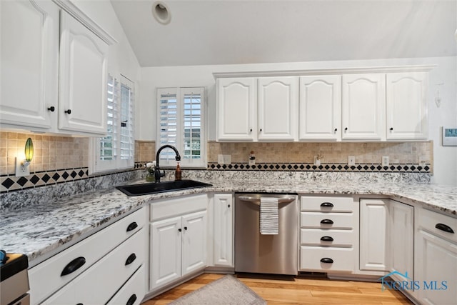 kitchen featuring decorative backsplash, stainless steel dishwasher, vaulted ceiling, sink, and white cabinetry