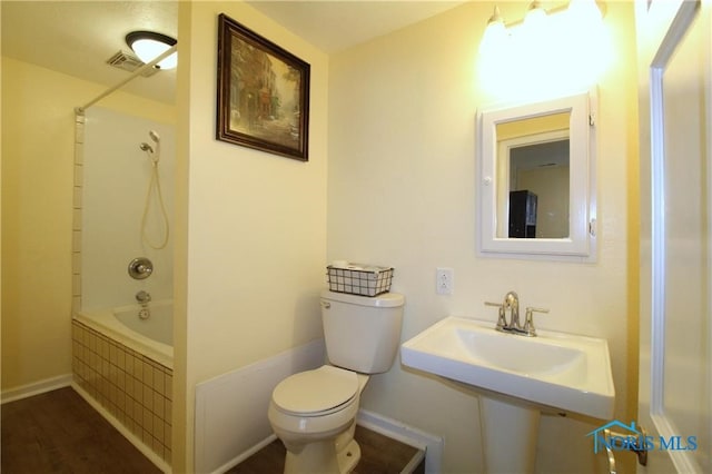 bathroom with hardwood / wood-style flooring, toilet, and tiled shower / bath combo