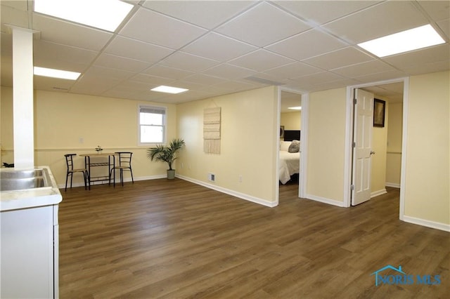 basement with dark wood-type flooring, a paneled ceiling, and sink