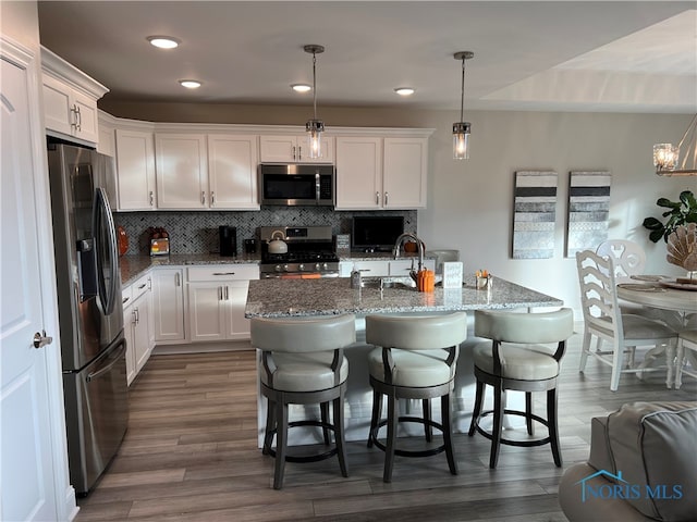 kitchen with stainless steel appliances, dark wood-type flooring, white cabinetry, and decorative light fixtures