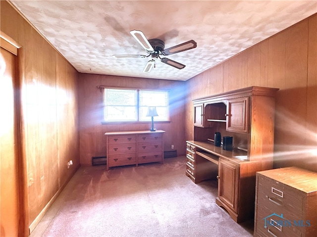 carpeted office space featuring wood walls, ceiling fan, built in desk, a textured ceiling, and a baseboard radiator