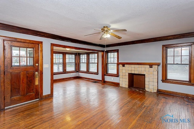 unfurnished living room with hardwood / wood-style flooring, plenty of natural light, ornamental molding, and a tiled fireplace