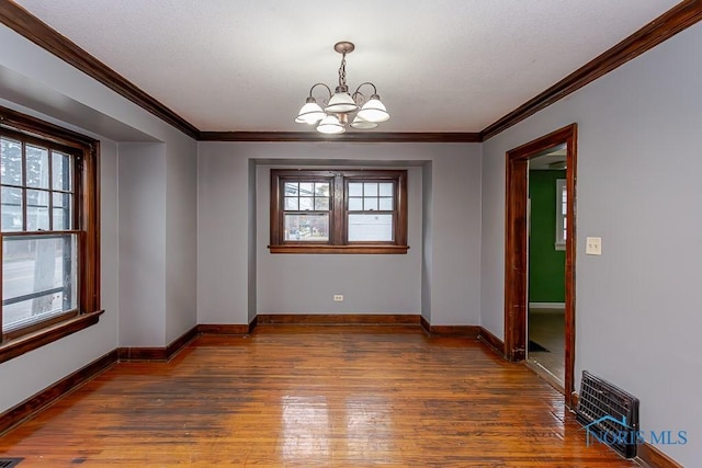 unfurnished dining area featuring a textured ceiling, dark hardwood / wood-style floors, crown molding, and a notable chandelier