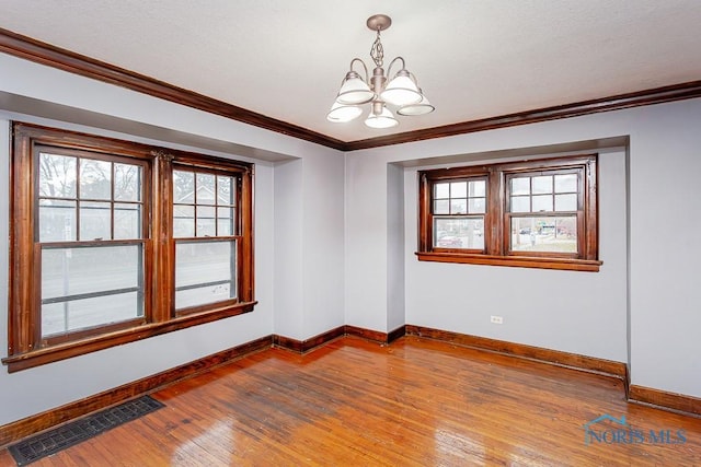 spare room with a wealth of natural light, hardwood / wood-style flooring, crown molding, and an inviting chandelier