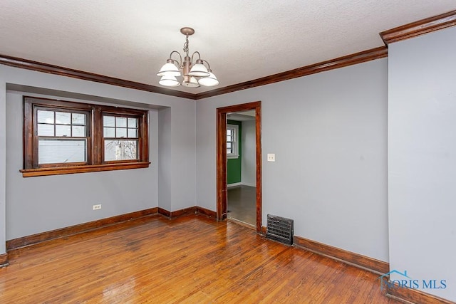 spare room with hardwood / wood-style floors, ornamental molding, a textured ceiling, and an inviting chandelier