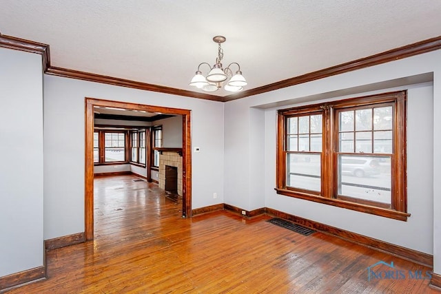 unfurnished room featuring a fireplace, hardwood / wood-style floors, an inviting chandelier, and ornamental molding